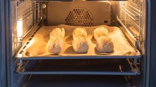 Brötchen liegen auf einem mit Backpapier belegten Blech im Backofen. Wie nachhaltig sind Brötchen zum Aufbacken im Vergleich zu solchen vom Bäcker? Sollte man sie im Backofen oder auf dem Toaster aufbacken?