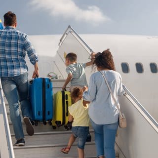 Eine vierköpfige Familie steigt die Treppen zum Flugzeugeinstieg hoch. Was tun bei Flugverspätungen oder Problemen mit Hotel oder Ferienwohnung? Wie bekommt man sein Geld zurück? Reiserecht