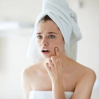Eine Frau entdeckt Pickel auf ihrer Haut. Ist basische Kosmetik gut für die Haut oder womöglich sogar schädlich? Was braucht die Haut an Pflege?