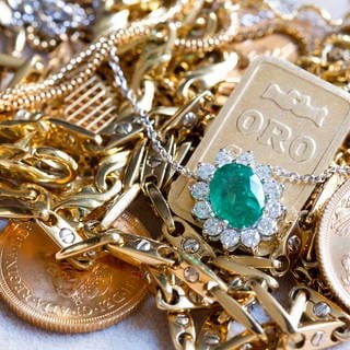 In einer Nahaufnahme liegen goldene Münzen, Ketten und Armreifen auf einem Haufen. Grün unterlegt steht der Titel: Schmucl, Münzen & Co.:Wie Fair geht es beim Goldankauf zu?