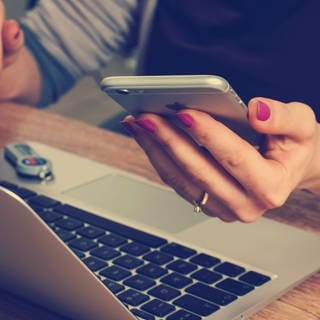 Betrug beim Online-Banking: Wer zahlt für den Schaden, wenn Kriminelle das Konto räumen. Eine Frau sitzt vor einem Laptop, in der linken Hand hält sie ein Smartphone.