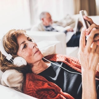 Digitales Erbe, digitaler Nachlass: Frau liegt mit Smartphone auf dem Sofa.