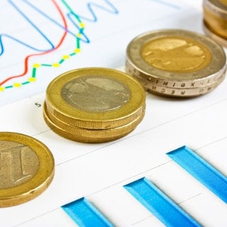 Euromünzen und Diagramme: Die Inflationsrate sinkt, aber wie lange noch?