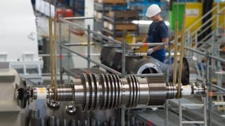 Ein Arbeiter steht in einer Montagehalle des Siemens-Turbinenwerks. Im Vordergrund hängt eine Turbine in der Montage.
