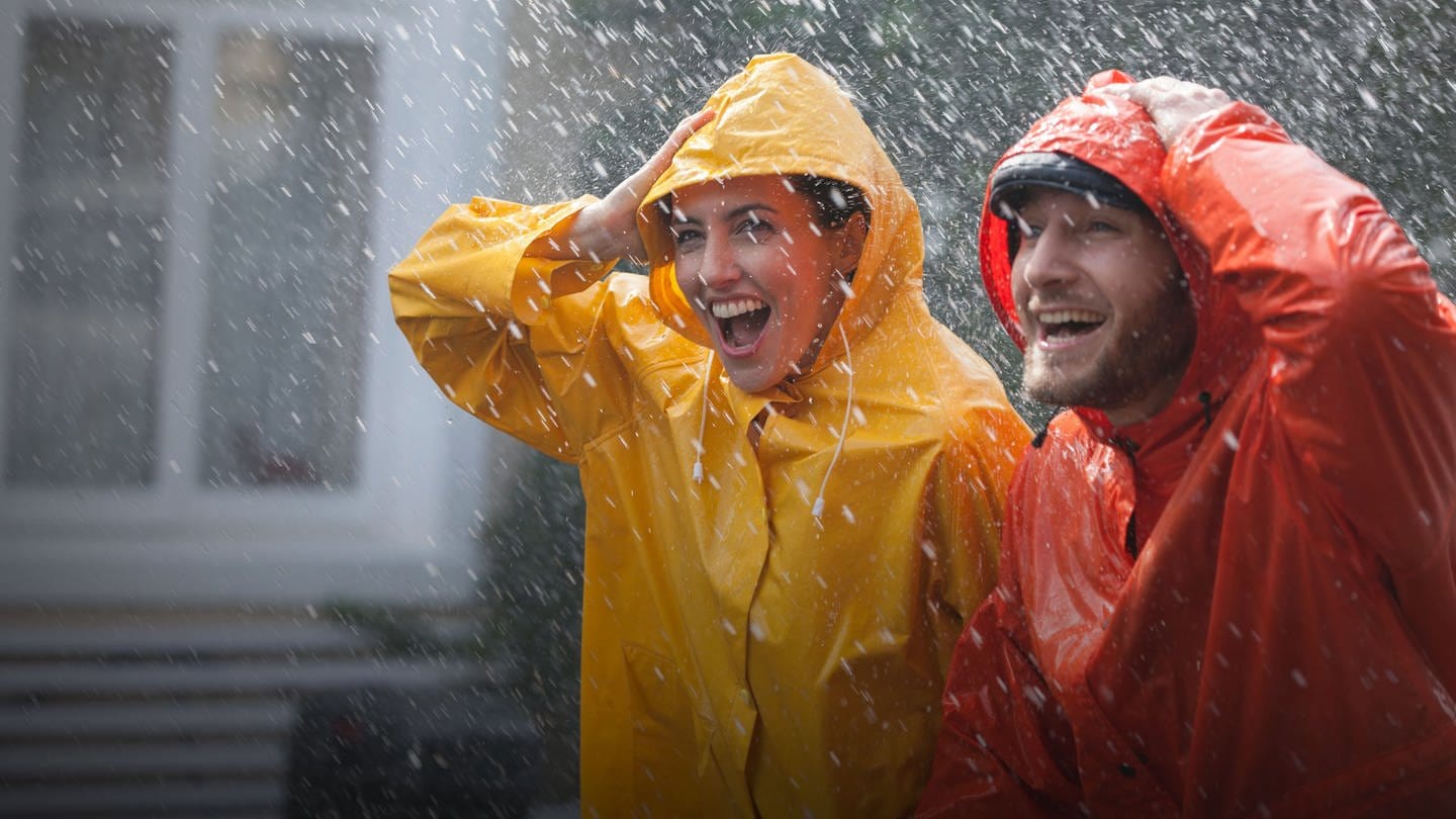 Zwei Personen stehen im Regen in einer gelben und roten Regenjacke. Sicher und trocken durch den Regen?