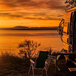 Wohnmobil und Campingstühle vor einem See