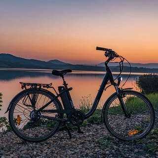 Ein E-Bike steht vor einem See bei Sonnenuntergang. Akkus: Brandgefahr und Entsorgung.