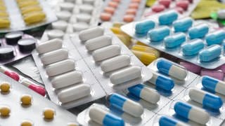 Verschiedene Blister mit weißen und bunten Tabletten und Kapseln liegen auf einem Tisch. Helfen Probiotika wirklich der Gesundheit?