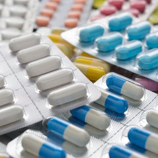 Verschiedene Blister mit weißen und bunten Tabletten und Kapseln liegen auf einem Tisch. Helfen Probiotika wirklich der Gesundheit?