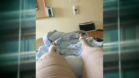 Eine Person liegt mit vollständig verbundenen Beinen in einem Krankenbett.