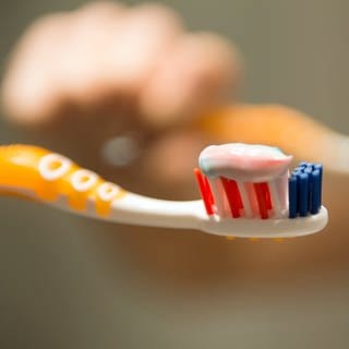 Eine Hand hält eine Zahnbürste mit Zahnpasta vor einem Spiegel. 