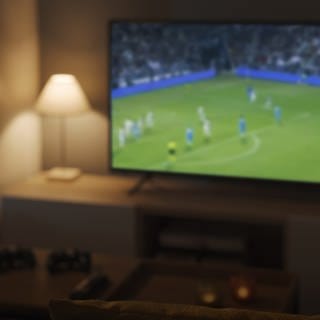 Fernseher in einem Wohnzimmer auf welchem Fußball läuft. TV: Fernseher neu kaufen oder Sound aufrüsten zur EM.