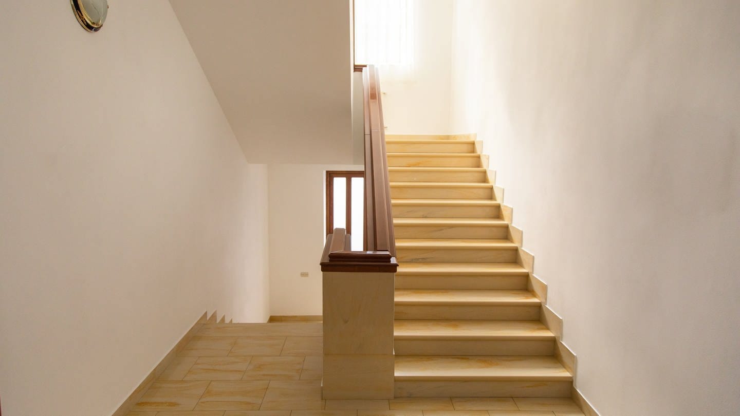Ein Treppenhaus mit einer Treppe, welche nach unten und oben führt und zwei Hände, die einen Geldbeutel mit wenigen Münzen halten. Verpasste Widerrufsfrist: Nie installierter Treppenlift wird teuer.