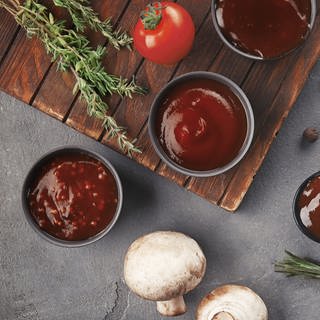 Auf einem Holzbrett mit Rosmarin, Tomate und Pilzen angerichtet: Dunkelrote süß-saure Soße. Marktcheck hat das Rezept.