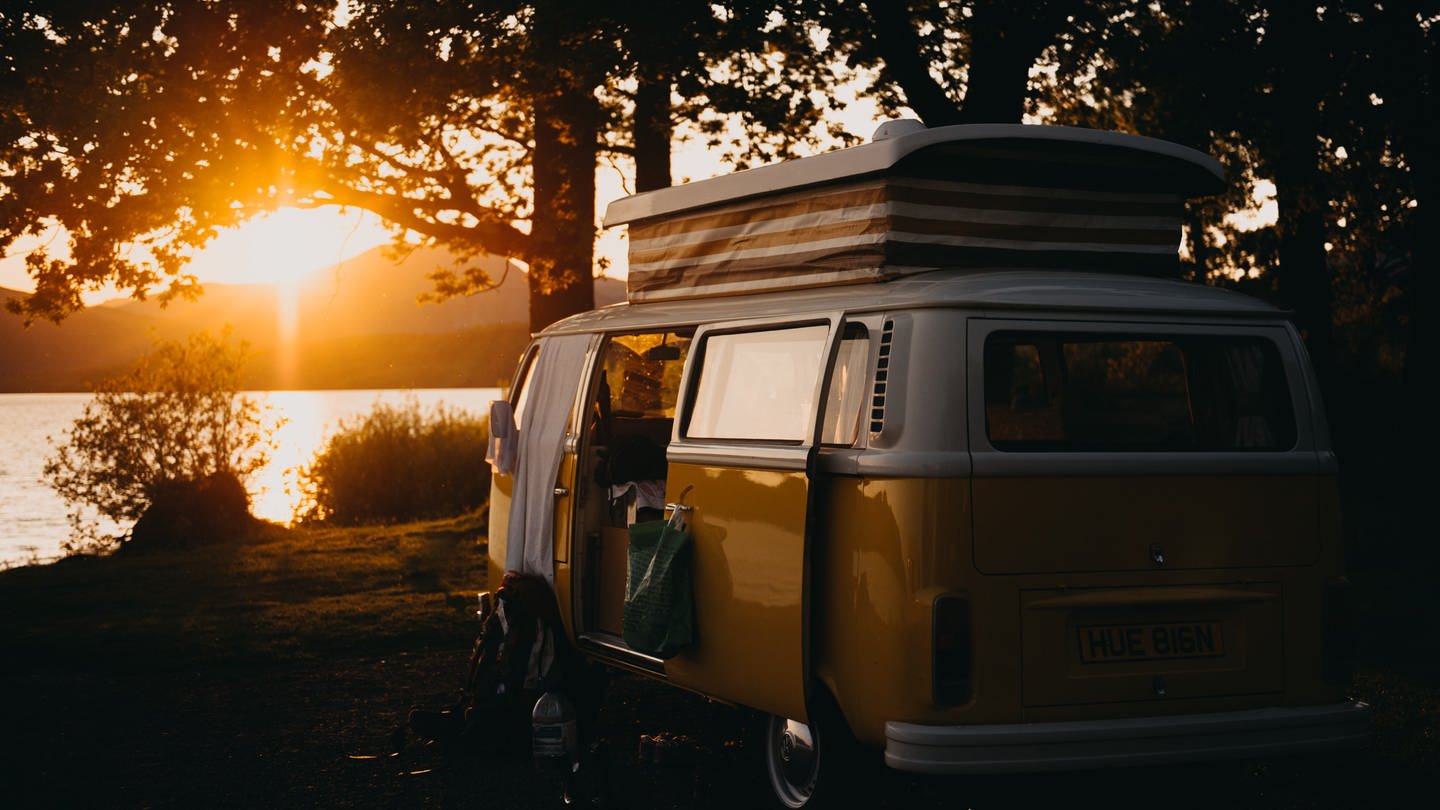 Alter Camperbus mit englischem Kennzeichen steht an einem See während die Sonne untergeht. Wie ist man auf Reisen mit Wohnmobil und Camper besonders nachhaltig und umweltfreundlich unterwegs?