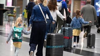 Kinder und Erwachsene mit Koffern und Rucksäcken in einer Flughafenhalle