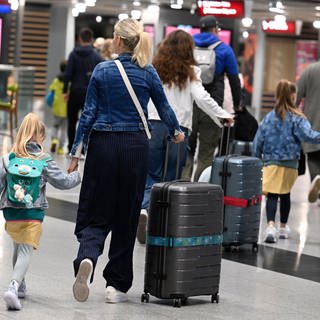 Kinder und Erwachsene mit Koffern und Rucksäcken in einer Flughafenhalle