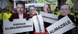 Eine Protestaktion von Deutscher Umwelthilfe und BUND bei der Teilnehmer Masken mit Bildern von Politikern tragen 
