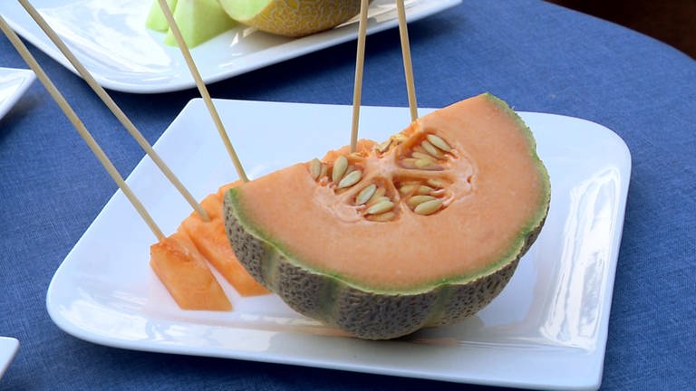 Aufgeschnittene Cantaloupe-Melone mit orangenem Fruchtfleisch und gerippter Schale. Alles Wissenswerte zu Honigmelonen, Zuckermelonen, Wassermelonen, Galia-, Netzmelone und Cantaloupe