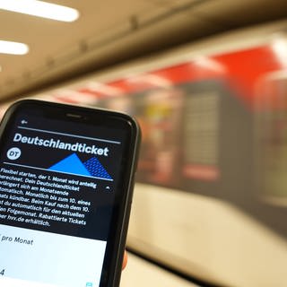 Hand hält Deutschlandticket auf Smartphone an einem Bahnhof. Betrug mit Deutschlandtickets: Gauner nutzen Sicherheitslücken im SEPA-Lastschriftverfahren.