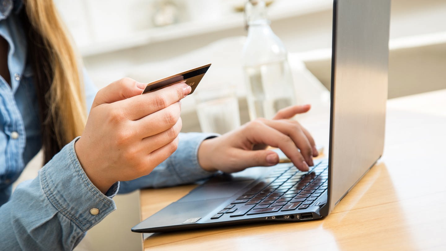 Eine Frau sitzt mit einer Kreditkarte in der Hand vor dem aufgeklappten Laptop