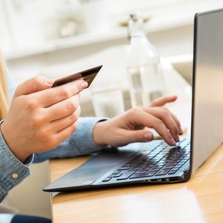 Eine Frau sitzt mit einer Kreditkarte in der Hand vor dem aufgeklappten Laptop