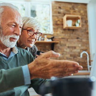 Ein älteres Paar schaut zufrieden auf einen Monitor. Hinzuverdienst in der Frührente: Welche finanziellen Vorteile habe ich?