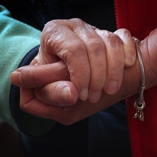 Auf dem Bild geben sich zwei Frauen stützend die Hand. Pflegebedürftig zu werden, ist ein Schicksalsschlag, der auch viele organisatorische Fragen aufwirft. In unserem Artikel erfahren Sie, wo es Beratung und Hilfe gibt und welche Leistungen in Frage kommen. 