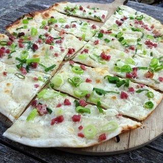 Auf einem Brettchen liegt ein geschnittener, klassischer Flammkuchen aus dem Tiefkühlregal.