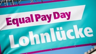 Bei einer Pressekonferenz hängt ein Banner mit der Aufschrift "Equal Pay Day - Lohnlücke". 