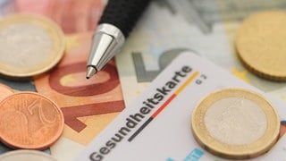 Gesundheitskarte liegt auf Geld. Die Zusatzbeiträge der Krankenkassen steigen 2025. Ist ein Wechsel jetzt sinnvoll?