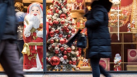 Eine Frau geht in der Innenstadt an einem weihnachtlich dekorierten Schaufenster entlang. 