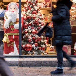 Eine Frau geht in der Innenstadt an einem weihnachtlich dekorierten Schaufenster entlang. 