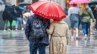 Ein Paar mit rotem Regenschirm beim Stadtbummel im Regen im September 2024.Unwetter haben 2024 nach erster Einschätzung der Versicherer in Deutschland weniger Schäden verursacht als im Jahr zuvor.