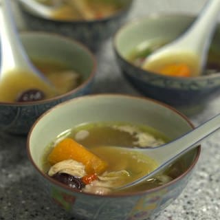 Vier asiatische Suppenschüsselchen gefüllt mit klarer Brühe