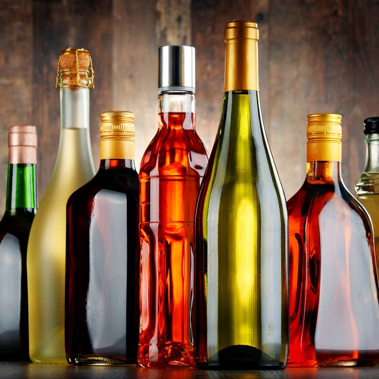 Glasflaschen verschiedene Sorten von Alkohol wie beispielsweise Sekt, Wein oder Rum stehen nebeneinander aufgereiht auf einem Tisch.
