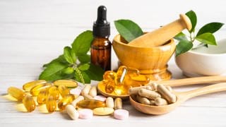 Zu sehen sin verschiedene Formen von Vitamin E Nahrungsergänzungsmitteln: Gelbe Pillen und Tropfen in einerm braunen Fläschchen. Es schützt Zellen vor oxidativem Stress und ist wichtig für das Immunsystem – Vitamin E. Wir zeigen neue Erkenntnisse dazu und zu Nahrungsergänzungsmitteln. 