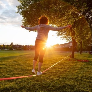 Eine Frau balanciert auf einer Slackline. Eine bessere Körperhaltung, geringere Sturzgefahr und weniger Rückenschmerzen: Balancetraining bringt viele positive Effekte mit sich. 