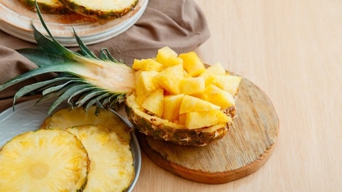 Geschnittene, gewürfelte Ananas in einer halbierten Ananas, daneben Ananas geschält und in Ringen. Ananas enthält neben Vitamin C auch gesunde Mineralstoffe, Magnesium, Eisen und Zink. Hilft das Superfood Obst auch beim Abnehmen?