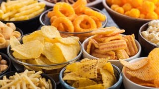 Chips, Salzbrezel, Sticks, Popcorn, Ringe und Nüsse in Schüsseln. Hunger und Appetit: Wie wir naschen, knabbern, snacken in den Griff bekommen. Essen ist überlebenswichtig und auch Genuss. Manchmal essen wir mehr als nötig und fühlen uns dennoch nicht satt. Neben der Ernährung sind soziale und psychologische Faktoren wichtig.