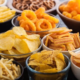 Chips, Salzbrezel, Sticks, Popcorn, Ringe und Nüsse in Schüsseln. Hunger und Appetit: Wie wir naschen, knabbern, snacken in den Griff bekommen. Essen ist überlebenswichtig und auch Genuss. Manchmal essen wir mehr als nötig und fühlen uns dennoch nicht satt. Neben der Ernährung sind soziale und psychologische Faktoren wichtig.