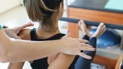 Eine Pilates Lehrerin unterstützt eine junge Frau bei der Ausführung der Pilates-Übung.