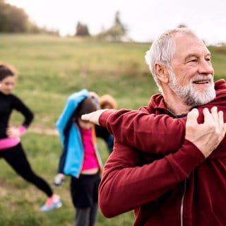 Ein älterer Mann macht Fitnessübungen, im Hintergrund ist eine Gruppe weiterer Sportler zu sehen.