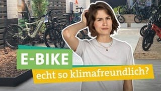 In der Bildmitte sieht man Ökocheckerin Katharina Röben. Sie blickt kritisch in die Kamera und fasst sich fragend an den Kopf. Vor ihr liest man "E-Bike", "echt so klimafreundlich?" hinterlegt mit farbigen Bändern. Im Hintergrund sieht man einen Verkaufsraum in dem verschiedene E-Bikes ausgestellt sind.
