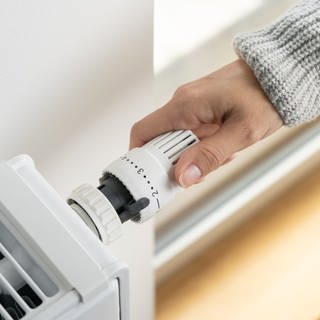Eine Person mit grauem Pulli greift von rechts das Thermostat einer Heizung, die auf Stufe 2 gestellt ist.