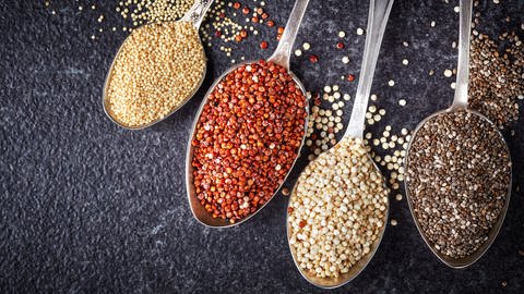 Die Superfoods Amaranth, dunkler und heller Quinoa und Chiasamen liegen auf Löffeln.