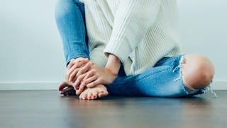Mädchen mit zerschlissenen Jeans sitzt auf dem Boden. Jeans im Used Look schaden in der Herstellung der Umwelt. Geht das auch nachhaltig?