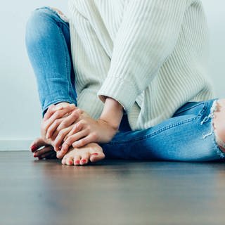 Mädchen mit zerschlissenen Jeans sitzt auf dem Boden. Jeans im Used Look schaden in der Herstellung der Umwelt. Geht das auch nachhaltig?