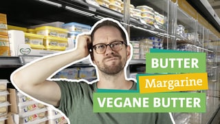 Ökochecker Tobias Koch fragt sich was die beste Wahl ist Butter, Margarine oder vegane Butter. Er fasst sich fragend an den Kopf. In der rechten Bildhälfte steht "Butter", "Margarine" und "Vegane Butter". Im Hintergrund ist ein mit verschiedenen Buttern und Butteralternativen gefülltes Kühlregal.