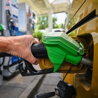 Eien Hand hält an einer Zapfsäuale an der Tankstelle einen grünen Tankrüssel in die Tankklappe, und betankt das Auto mit Kraftstoff.
